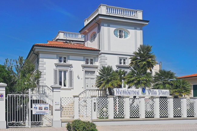 Villa bianca con palme e recinzione decorativa.