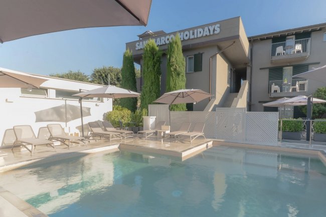 Piscina con sdraio e ombrelloni, edificio sullo sfondo.