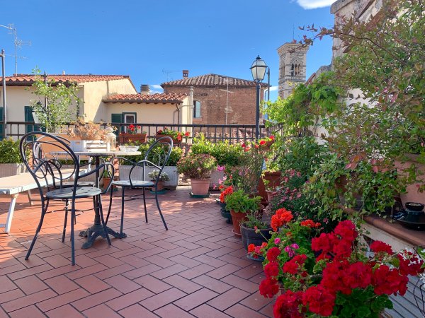Terrazza con tavolo, sedie e fiori colorati sotto un cielo azzurro.