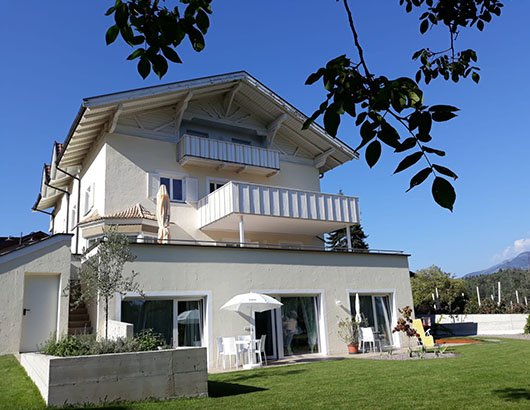 Casa bianca a tre piani con balconi e giardino.