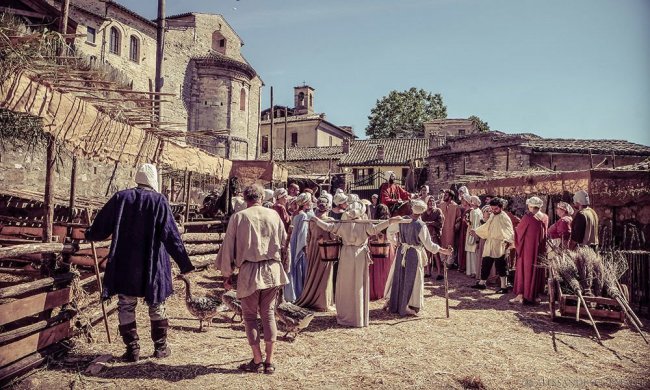 Scena medievale in costume con persone in un villaggio storico.