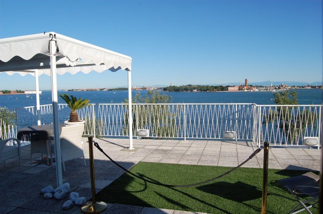 Terrazza con vista sul mare, tenda bianca e vegetazione.