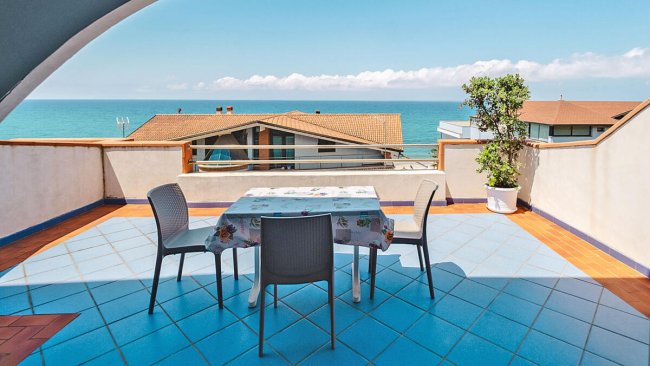 Terrazza sul mare con tavolo coperto e quattro sedie.