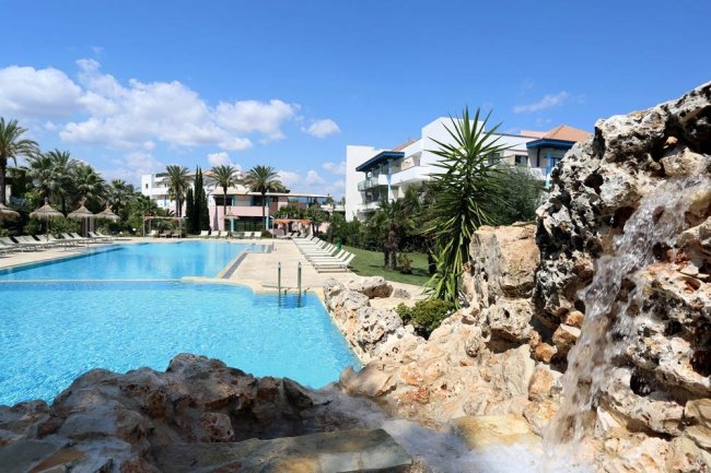 Piscina esterna con palme e edifici sullo sfondo.