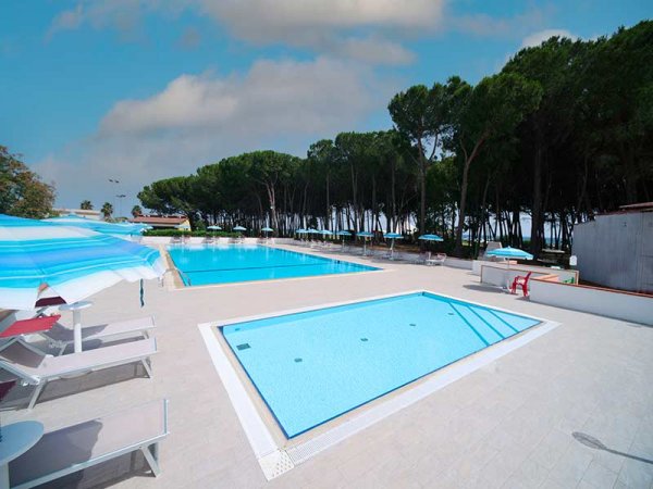 Due piscine all'aperto con ombrelloni e alberi attorno.