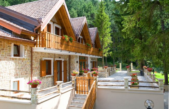Balconi fioriti su chalet in pietra nel bosco.