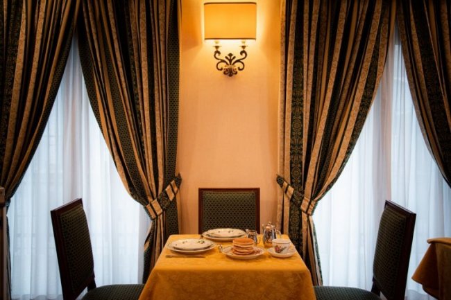 Tavolo apparecchiato in sala elegante con tende.