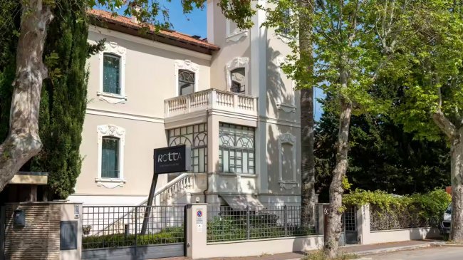 Edificio bianco elegante con un'insegna nera tra alberi.