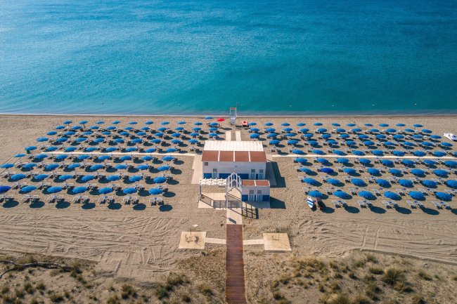 Spiaggia con ombrelloni blu e cabina centrale.
