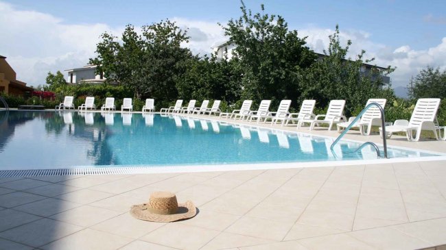 Una piscina con lettini bianchi e un cappello di paglia.