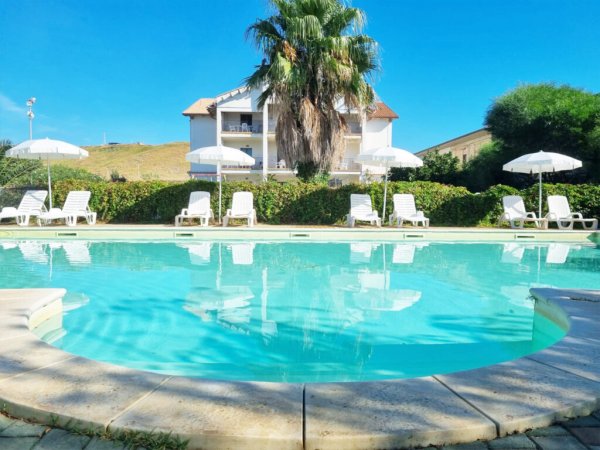 Piscina con lettini e ombrelloni, edificio sullo sfondo.