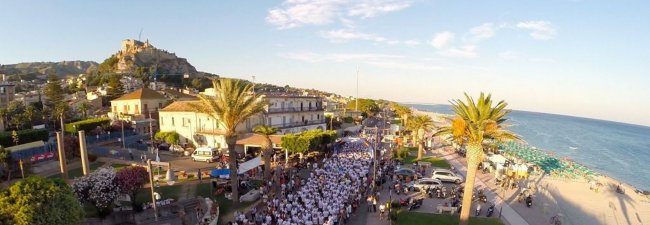 Spiaggia e strada con palme, folla in bianco, edificio storico in lontananza.
