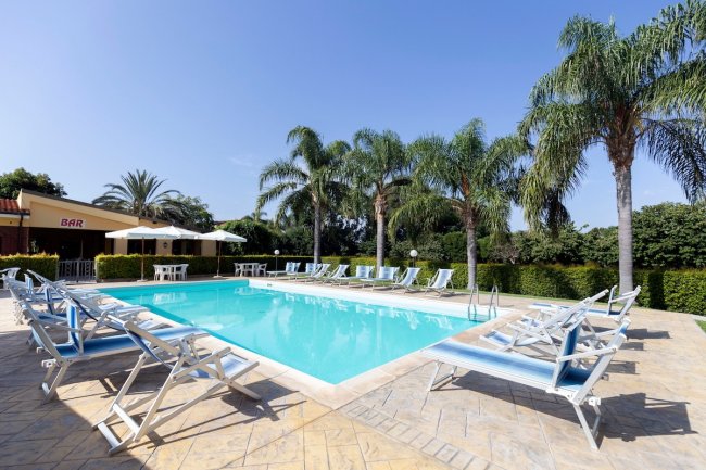 Piscina all'aperto con lettini e palme.