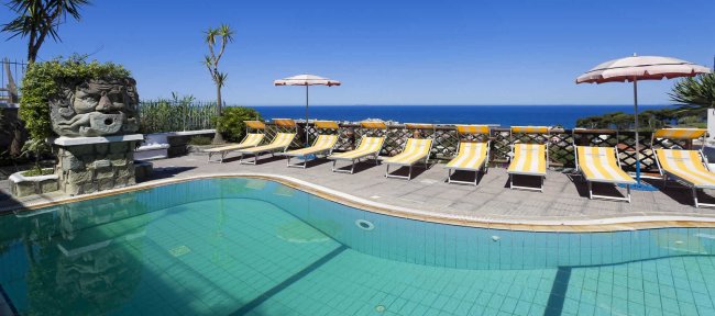 Piscina all'aperto con sdraio e vista mare.