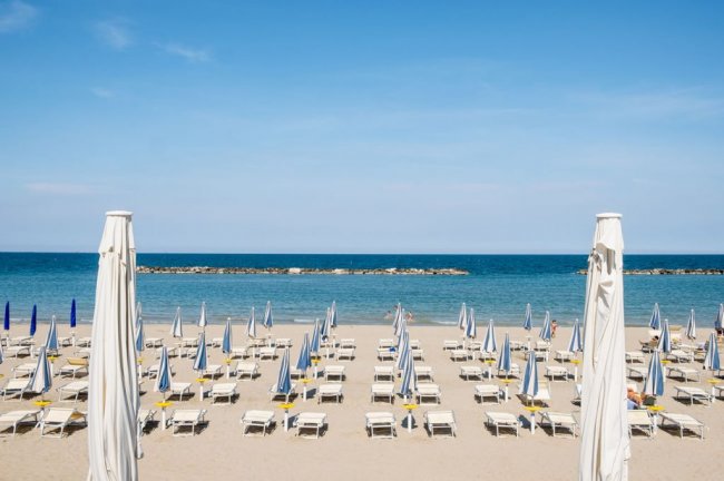 Spiaggia con lettini e ombrelloni, mare all'orizzonte.
