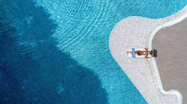 Persona che prende il sole accanto a una piscina blu.