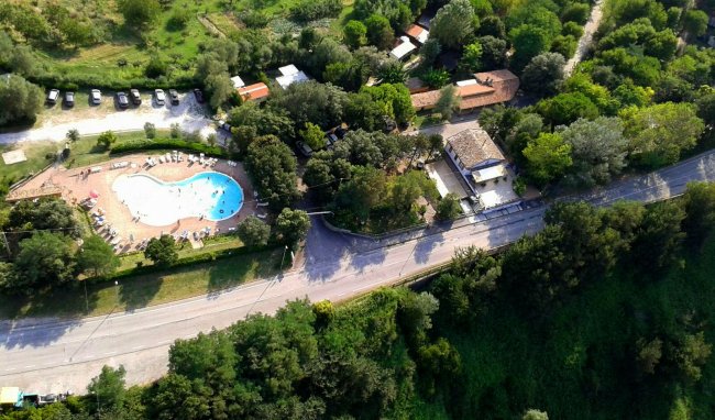 Vista aerea di un campeggio e piscina tra alberi.