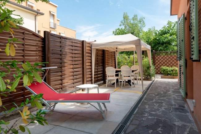Area esterna con lettino rosso e gazebo bianco.