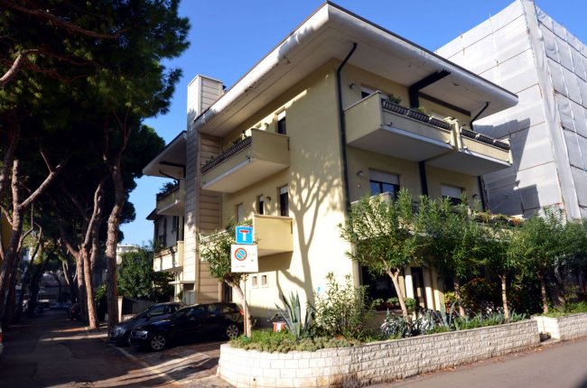 Edificio giallo a due piani con balconi e piante davanti.