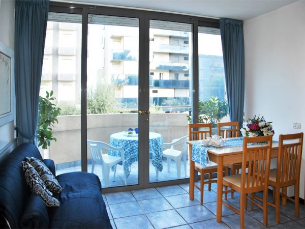 Soggiorno con divano blu, tavolo da pranzo e balcone.