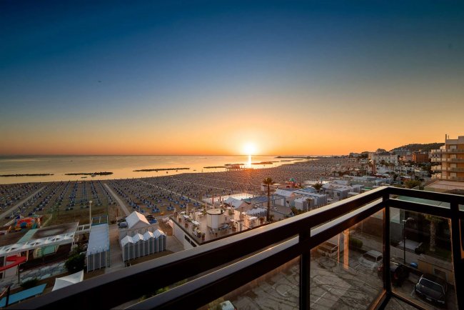 Tramonto visto da un balcone su una spiaggia affollata.