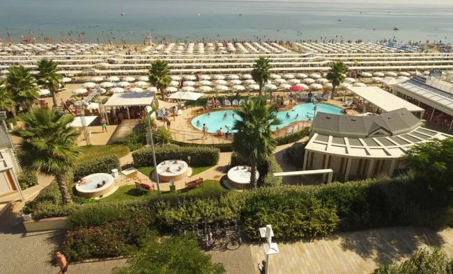 Spiaggia affollata con ombrelloni e piscina.
