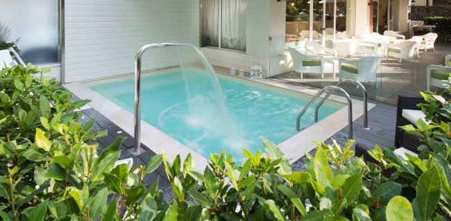 Una piccola piscina con cascata e sedie bianche.