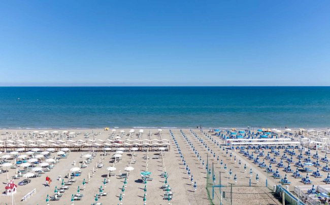 Spiaggia con ombrelloni ordinati e mare blu.