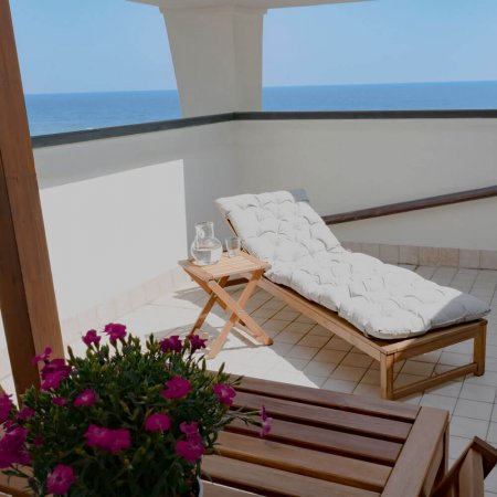 Terrazza vista mare con lettino e fiori rosa.
