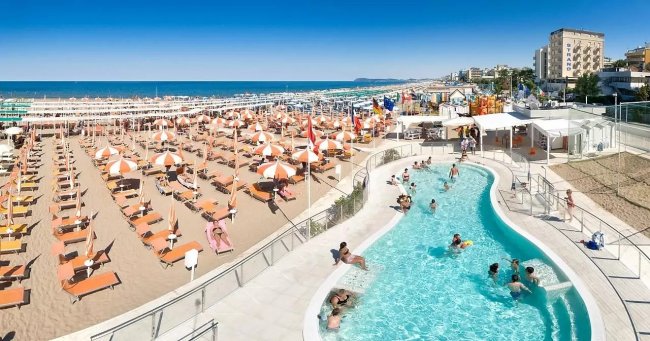 Spiaggia affollata con piscina e ombrelloni.