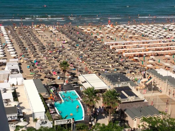 Spiaggia affollata con ombrelloni e piscina.