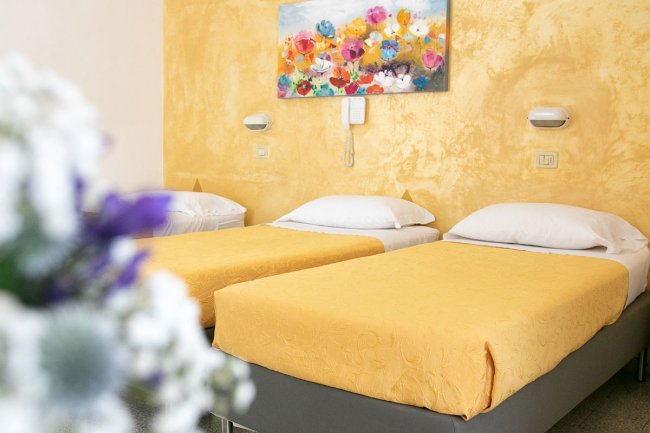 Due letti singoli con copriletto gialli, quadro floreale sopra.