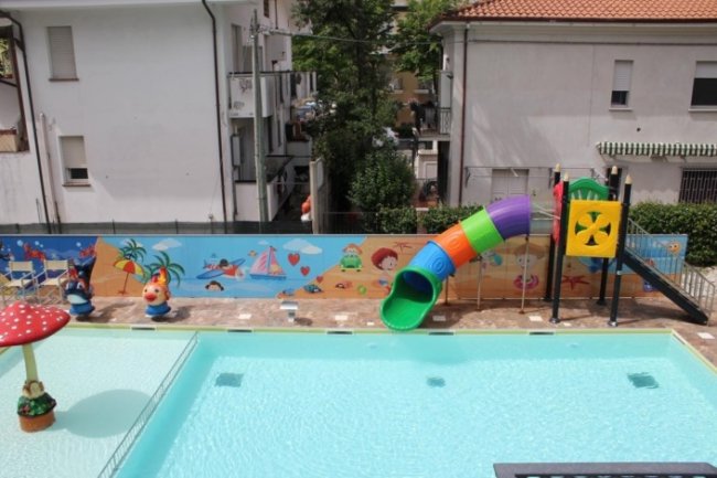 Piscina bassa con scivolo colorato e decorazioni murali.