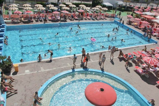 Piscina affollata con ombrelloni intorno.