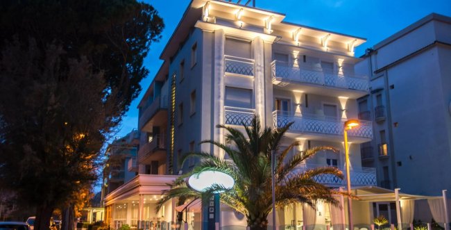 Edificio illuminato di sera con palme davanti.