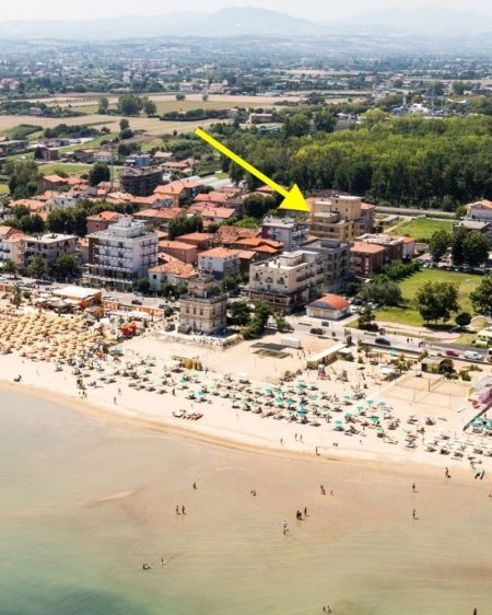 Spiaggia con ombrelloni e mare, freccia indica edificio.