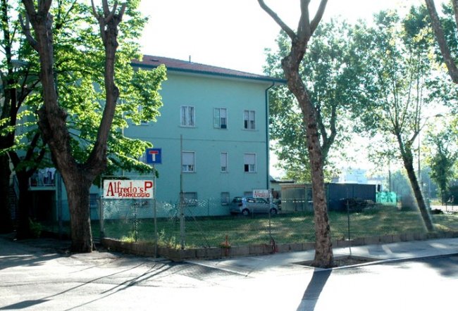 Edificio verde con parcheggio recintato alberato.
