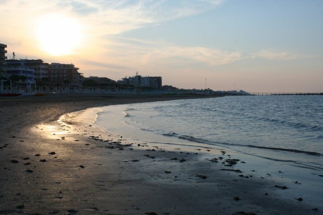Spiaggia al tramonto con edifici sullo sfondo.