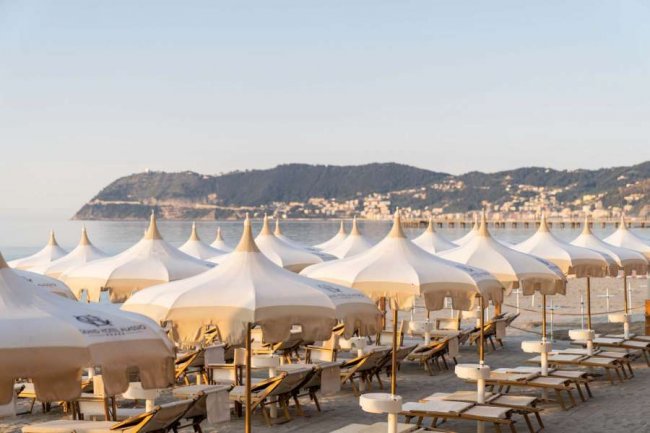 Spiaggia con ombrelloni e lettini, vista mare e colline.