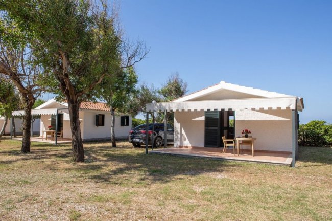 Bungalow con veranda, auto parcheggiata e alberi attorno.