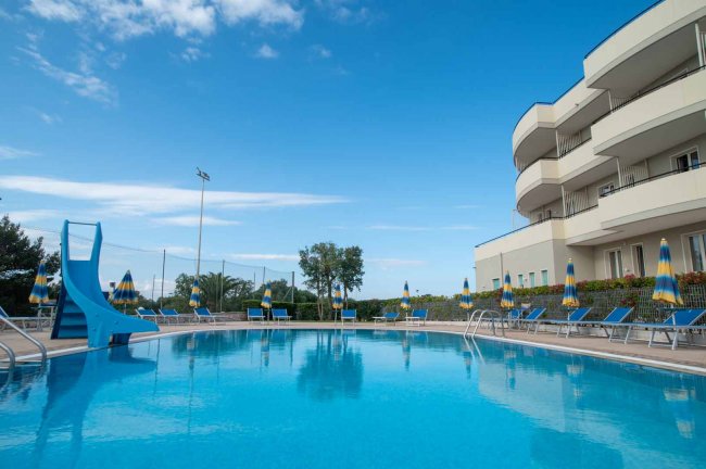 Piscina con scivolo blu e lettini con ombrelloni.