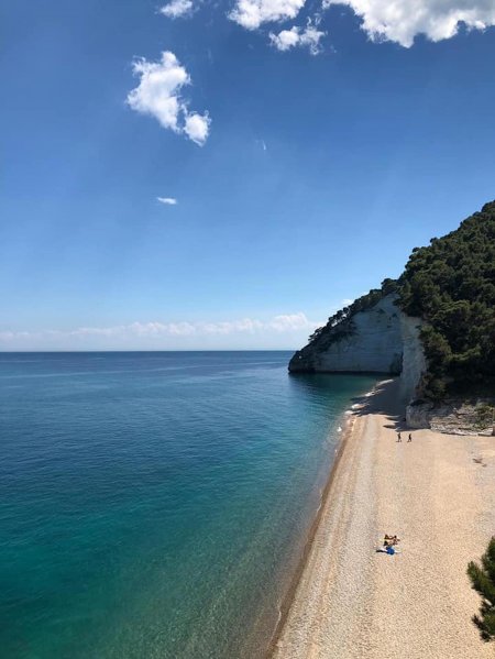 Spiaggia sabbiosa con mare calmo e scogliere.