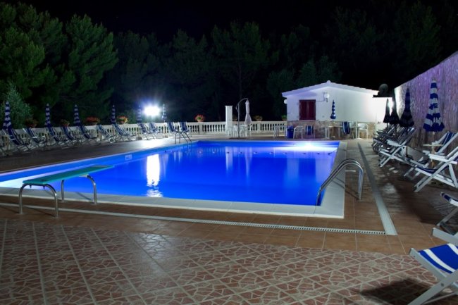 Piscina illuminata di notte, circondata da lettini.