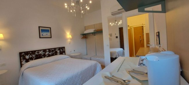 Stanza con letto matrimoniale, tavolo con bollitore e lampadario.