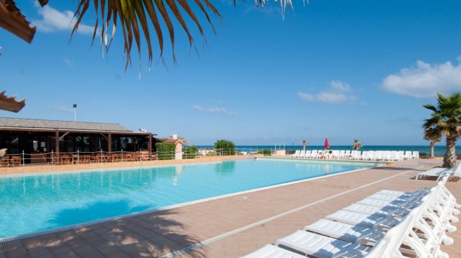 Piscina vista mare con lettini bianchi e palme.