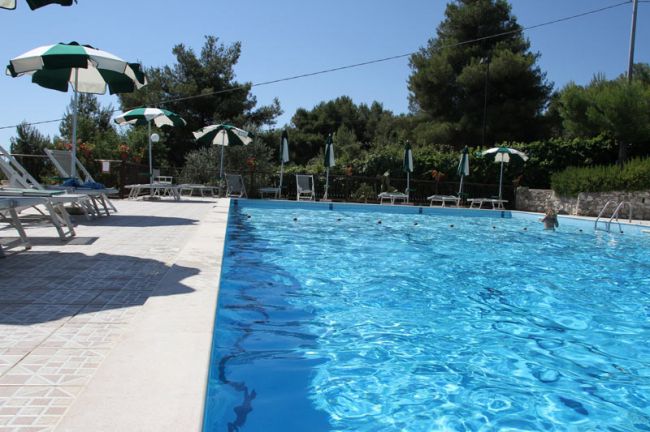 Ampia piscina con sdraio e ombrelloni a righe verdi e bianche.
