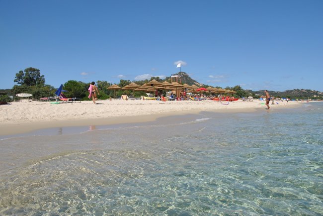 Spiaggia sabbiosa con ombrelli e colline sullo sfondo.
