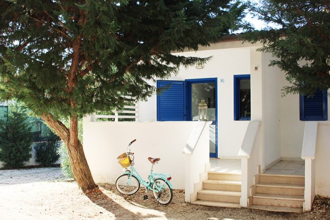 Casetta bianca con persiane blu e bici parcheggiata.