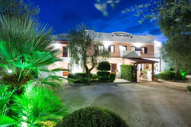 Un edificio bianco con ingresso e giardino illuminato di sera.