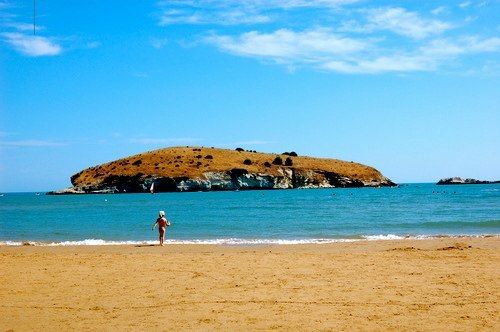Bambino sulla spiaggia con isola erbosa di fronte.